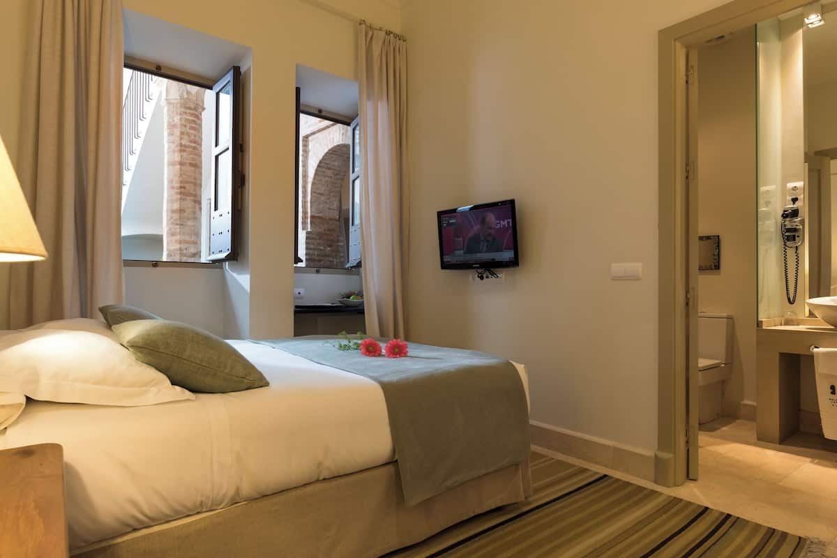 A hotel room with a bed, a television, a bathroom, and a window with curtains.