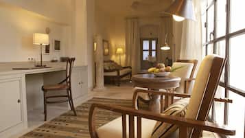 Une pièce confortable avec un bureau, des chaises, une table ronde sur laquelle sont disposés des fruits, et une grande fenêtre.