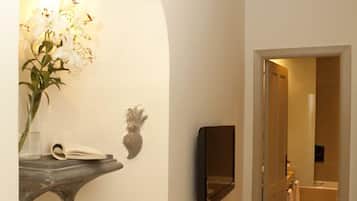 A hallway with a stone pedestal sink, a vase with flowers, a wall-mounted mirror, and a striped rug.