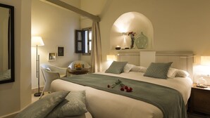 A bedroom with a large bed, a chair, a bedside table, a mirror, and a window with curtains.