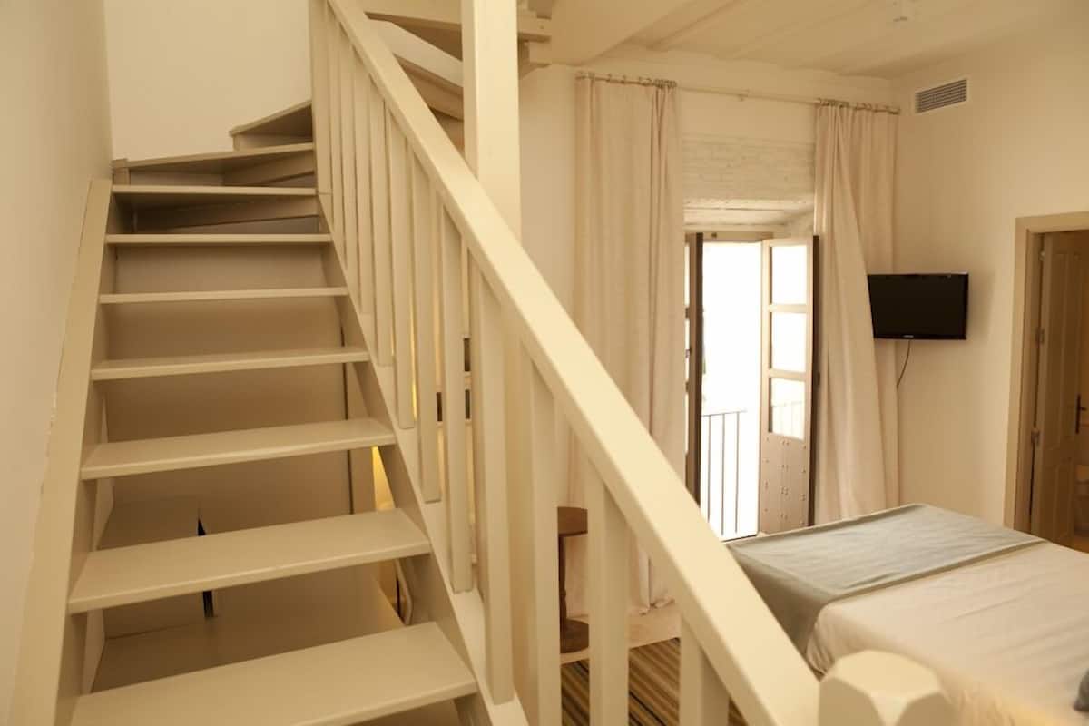 A bedroom with a bed, a TV mounted on the wall, and a staircase leading to another room.
