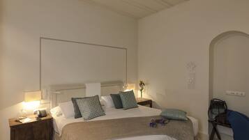 A hotel room with a bed, bedside tables, a lamp, a vase with flowers, and a wall-mounted light fixture.