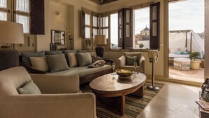 A cozy living room with a sofa, armchairs, a coffee table, and a view of the city through open doors.