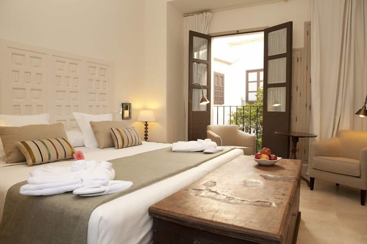 A hotel room with a bed, a wooden coffee table, a chair, and a view of the outside.