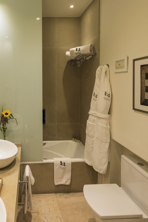 Un baño moderno con bañera, inodoro y lavamanos. Hay toallas y una bata colgadas en la pared.