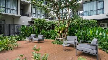 Un patio exterior moderno con piso de madera, sofás grises y abundante vegetación.