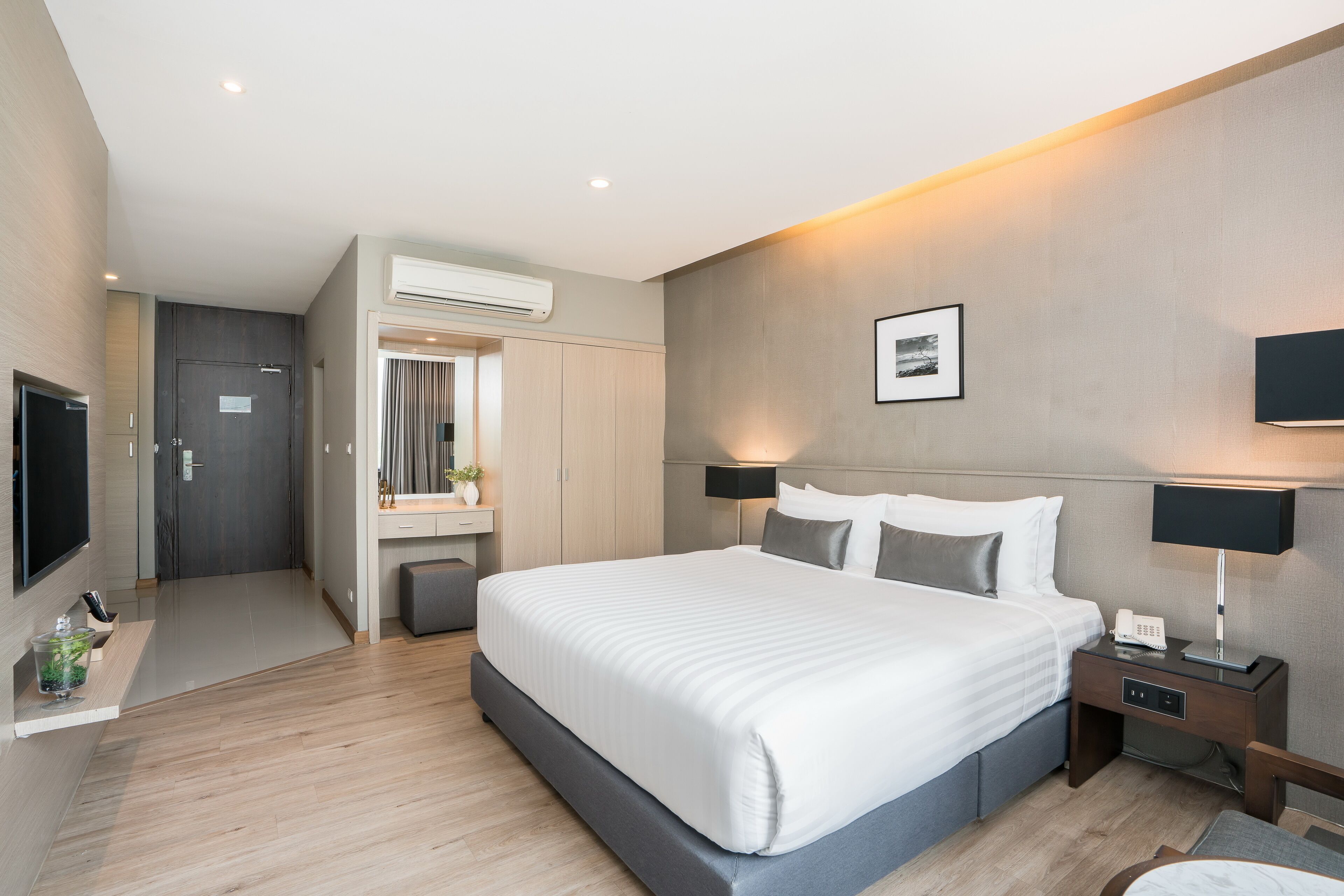 A modern hotel room with a large bed, bedside tables, a TV, and an air conditioning unit.
