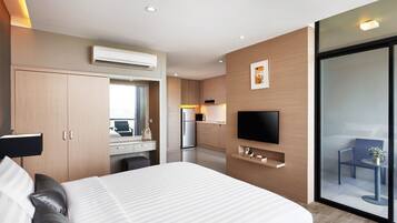 Una habitación de hotel moderna con una cama grande, un escritorio con computadora, televisor de pantalla plana, zona de cocina y puerta de vidrio corredera al balcón.