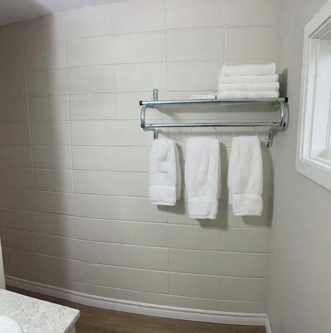 A bathroom with white tiled walls, a white sink, and a towel rack with folded towels.