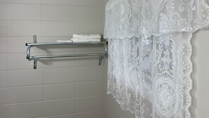 A bathroom with a white tiled wall, a towel rack with folded towels, and a decorative lace curtain. -  Inn On Pim (Sault Ste. Marie)