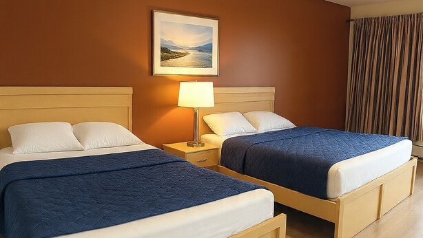 A hotel room with two beds, a nightstand, a lamp, and a painting on the wall. -  Inn On Pim (Sault Ste. Marie)