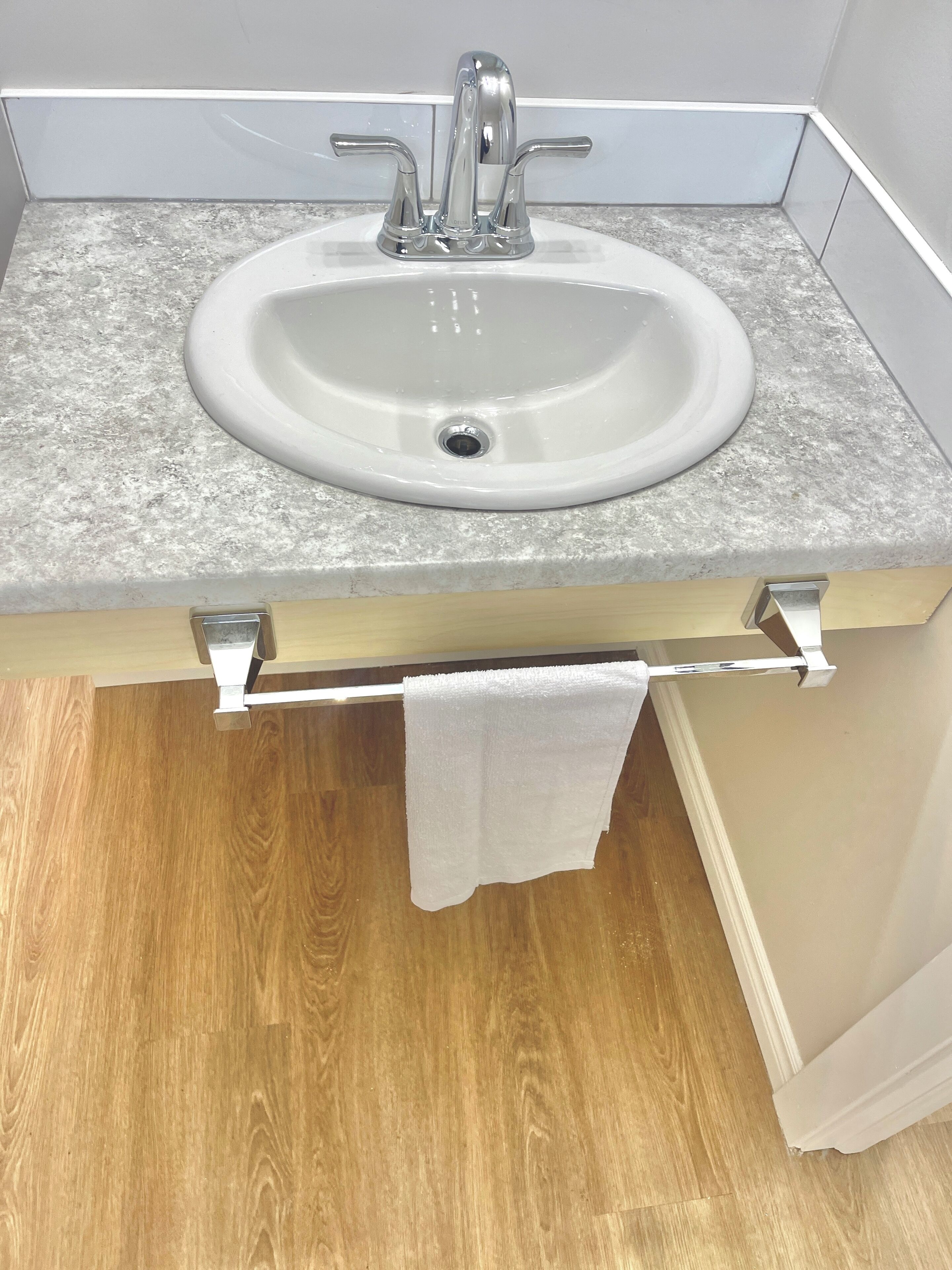Un baño con un lavamanos blanco, un perchero y suelo de madera.