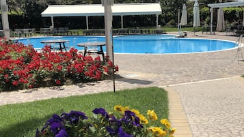 Un'area piscina con una zona relax coperta, una pergola bianca e un vaso con fiori.