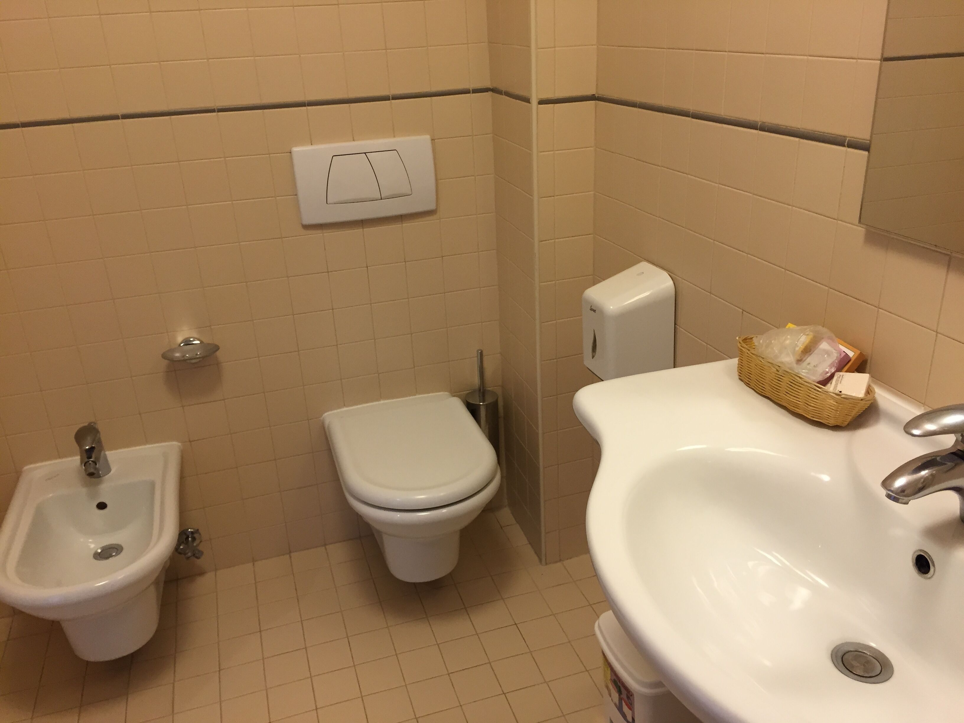 A bathroom with a bidet, toilet, sink, and a soap dispenser.