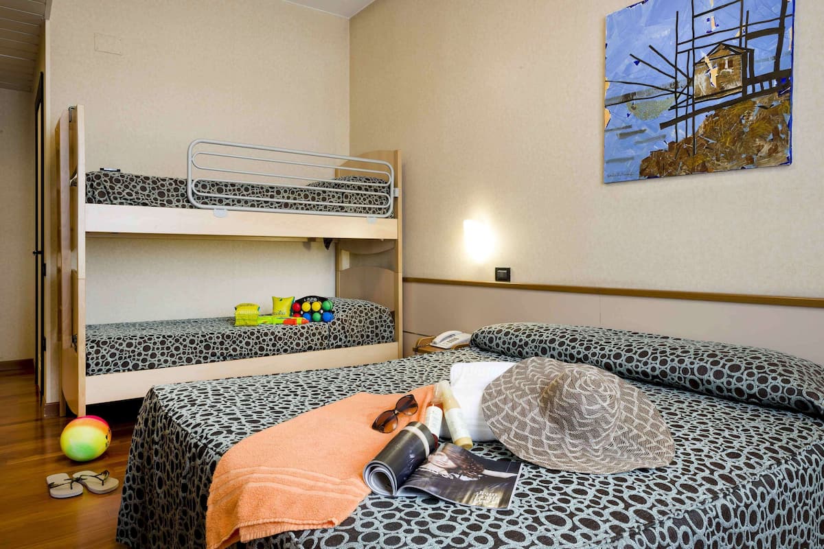 A bunk bed with patterned bedding, a small table with a magazine, and a wall-mounted painting.