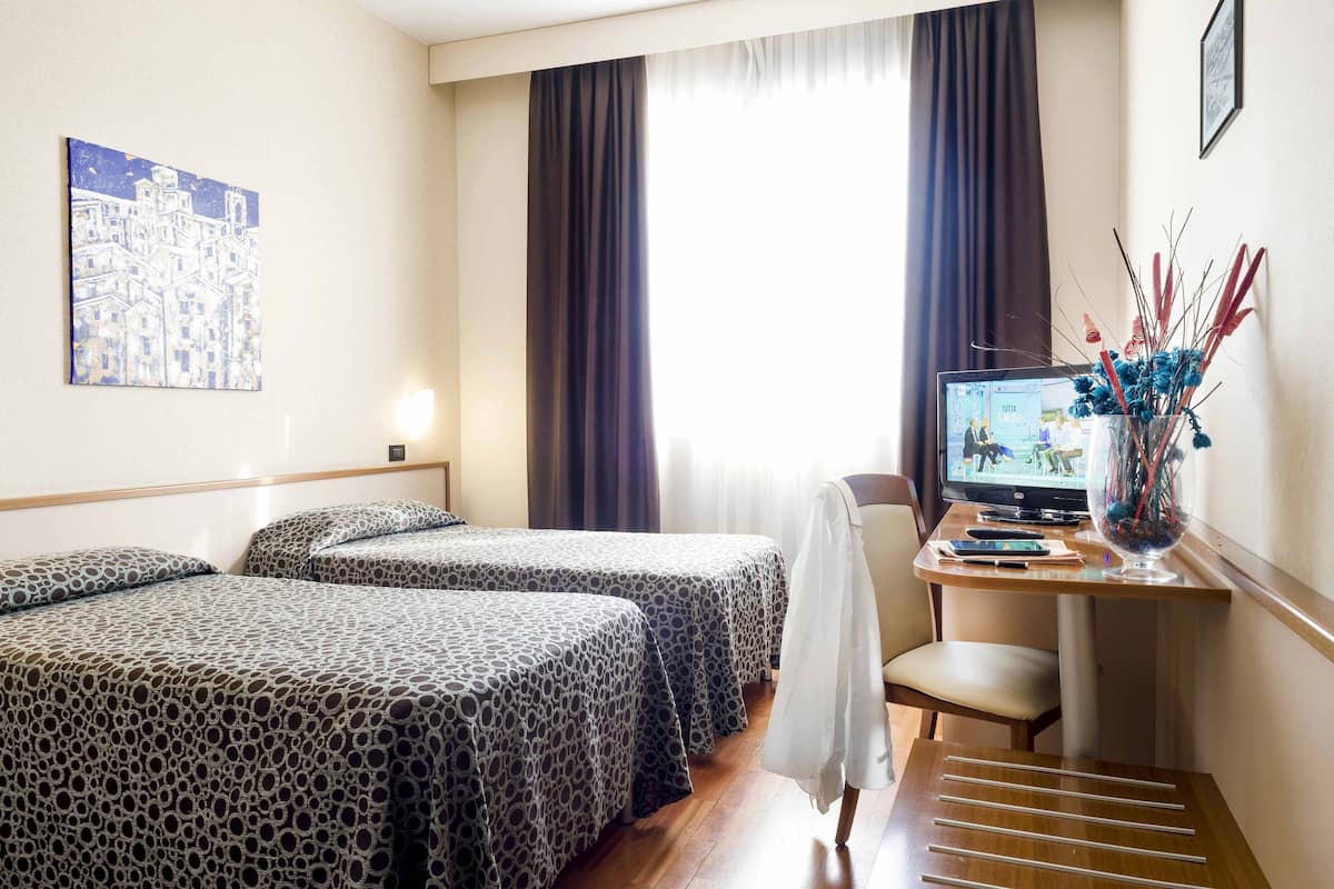 A hotel room with two beds, a desk with a computer, and a window with curtains.