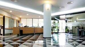 Vestíbulo de hotel con mostrador de recepción, un pilar grande y suelo a cuadros.
