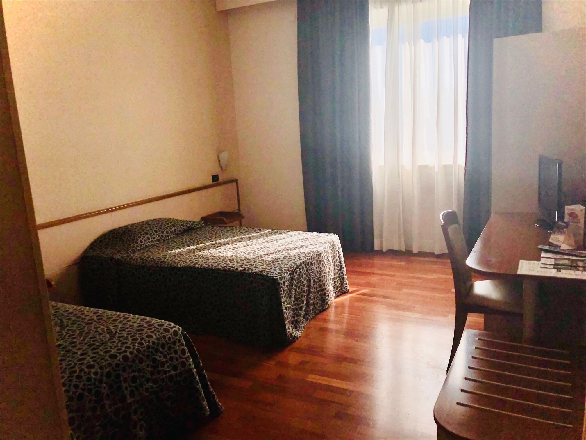 Quarto de hotel com duas camas, uma mesa de jantar de madeira e uma cadeira.