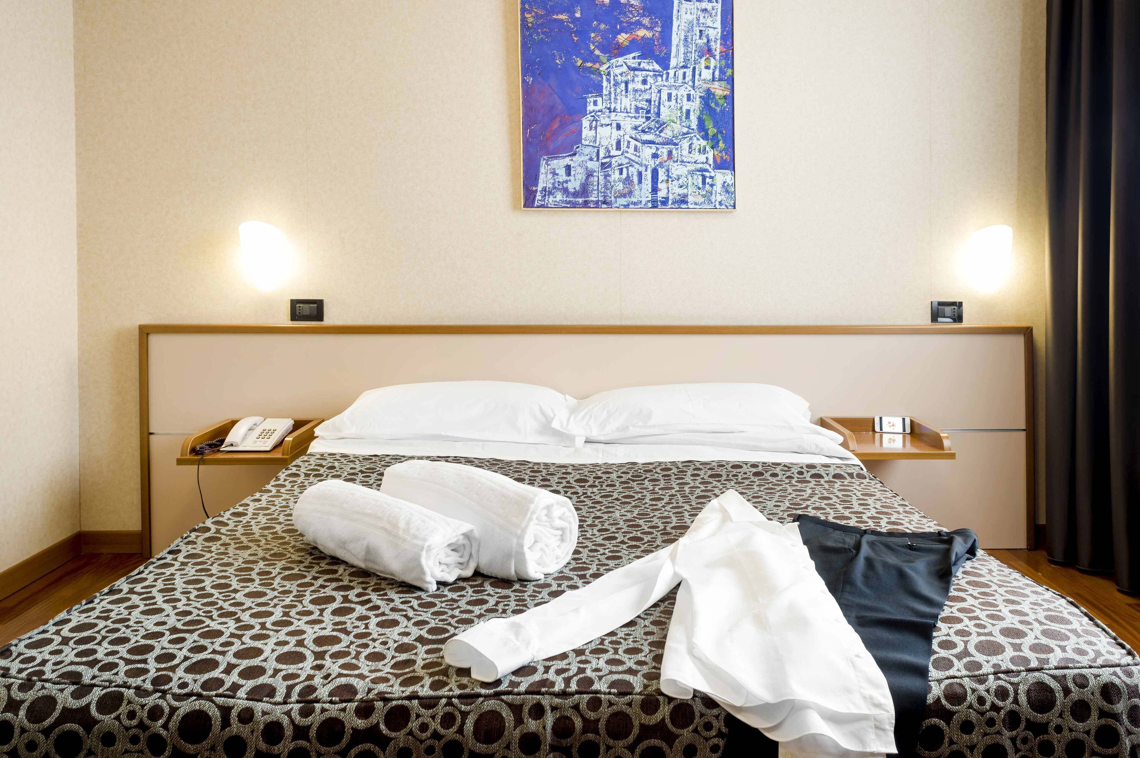 Una habitación de hotel con una colcha estampada, toallas dobladas con cuidado, un teléfono en la mesita de noche y un cuadro en la pared.