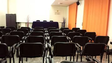 Un salón de conferencias con filas de sillas negras, una mesa con cubierta azul y una cortina naranja.
