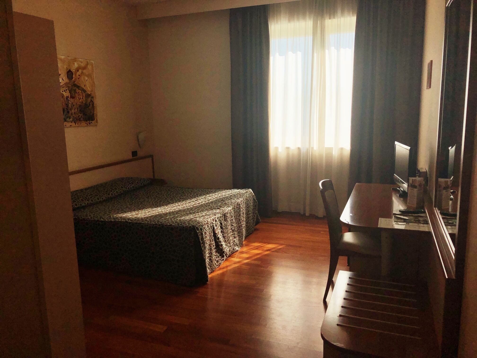 A hotel room with a bed, a desk, a chair, and a window with curtains.