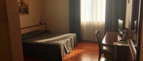 A hotel room with a bed, a desk, a chair, and a window with curtains.