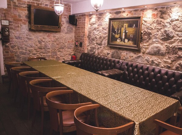 A long table with a patterned tablecloth, surrounded by wooden chairs, in a room with stone walls and a leather couch.