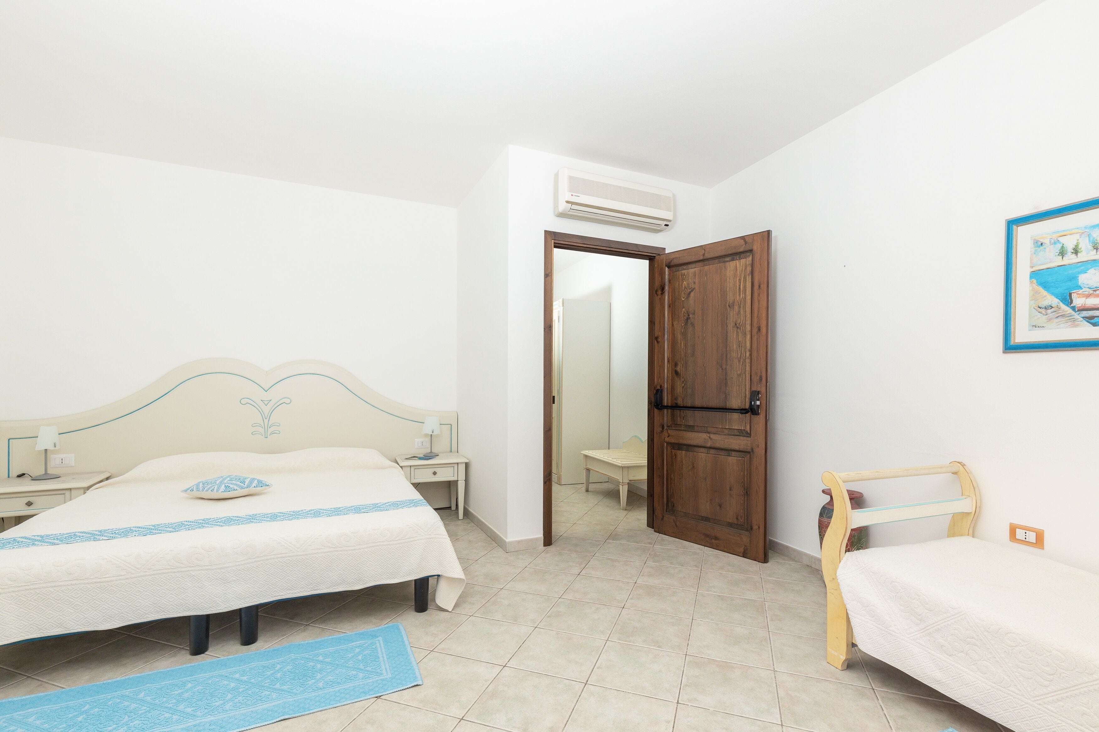 Une chambre avec deux lits, une porte en bois, une petite table et un climatiseur fixé au mur.