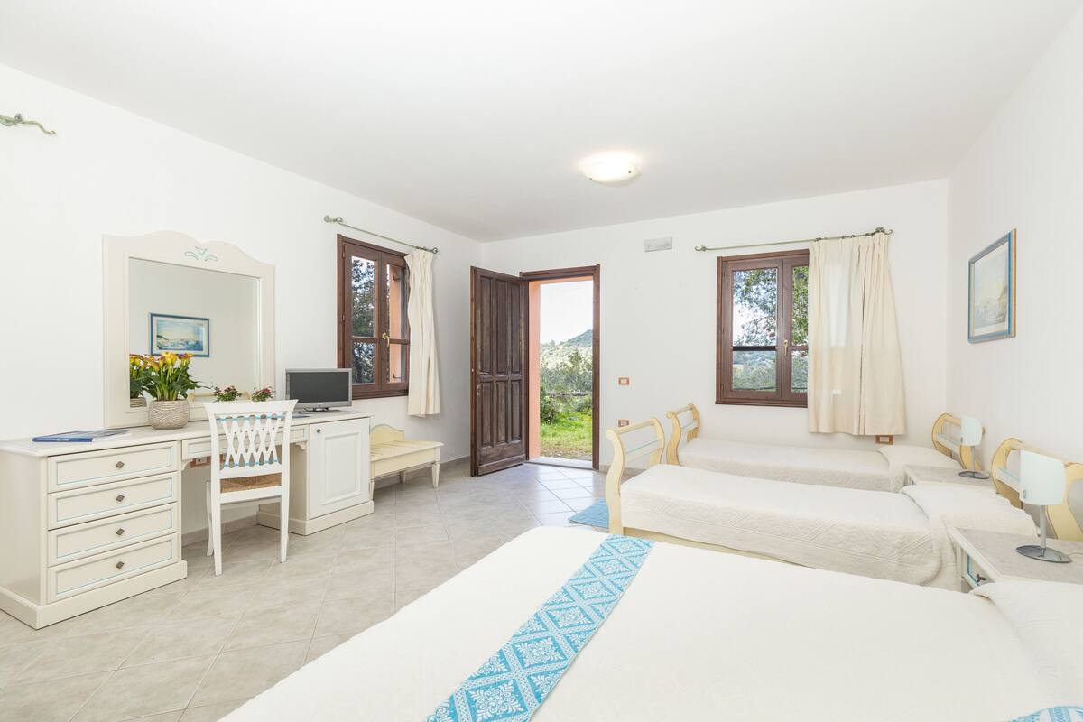 A bedroom with a desk, two beds, a chair, and a door leading to a balcony.