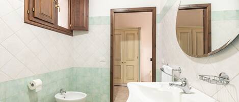 Een badkamer met toilet, bidet, wastafel en houten kastjes.