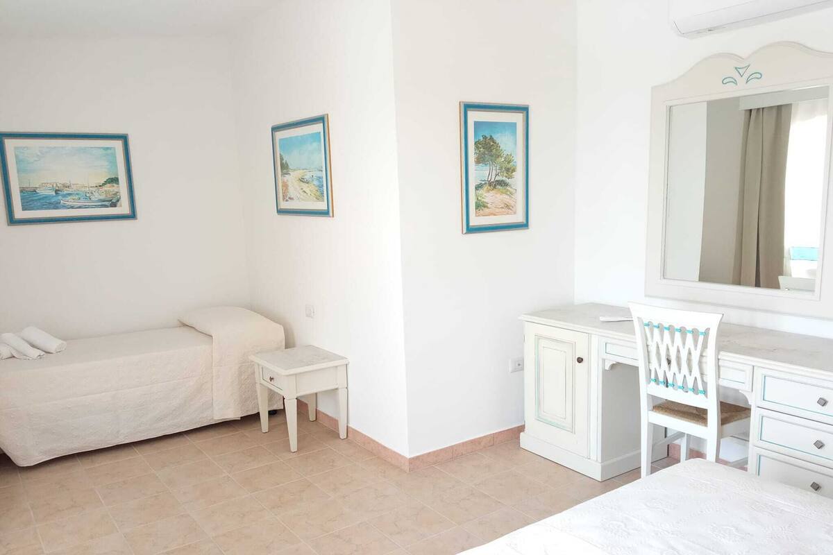 A bedroom with a bed, a bedside table, a chair, a dresser, and a large mirror. There are three framed pictures on the wall.