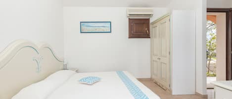 A bedroom with a bed, a nightstand, a wall-mounted air conditioner, a door, and a window.