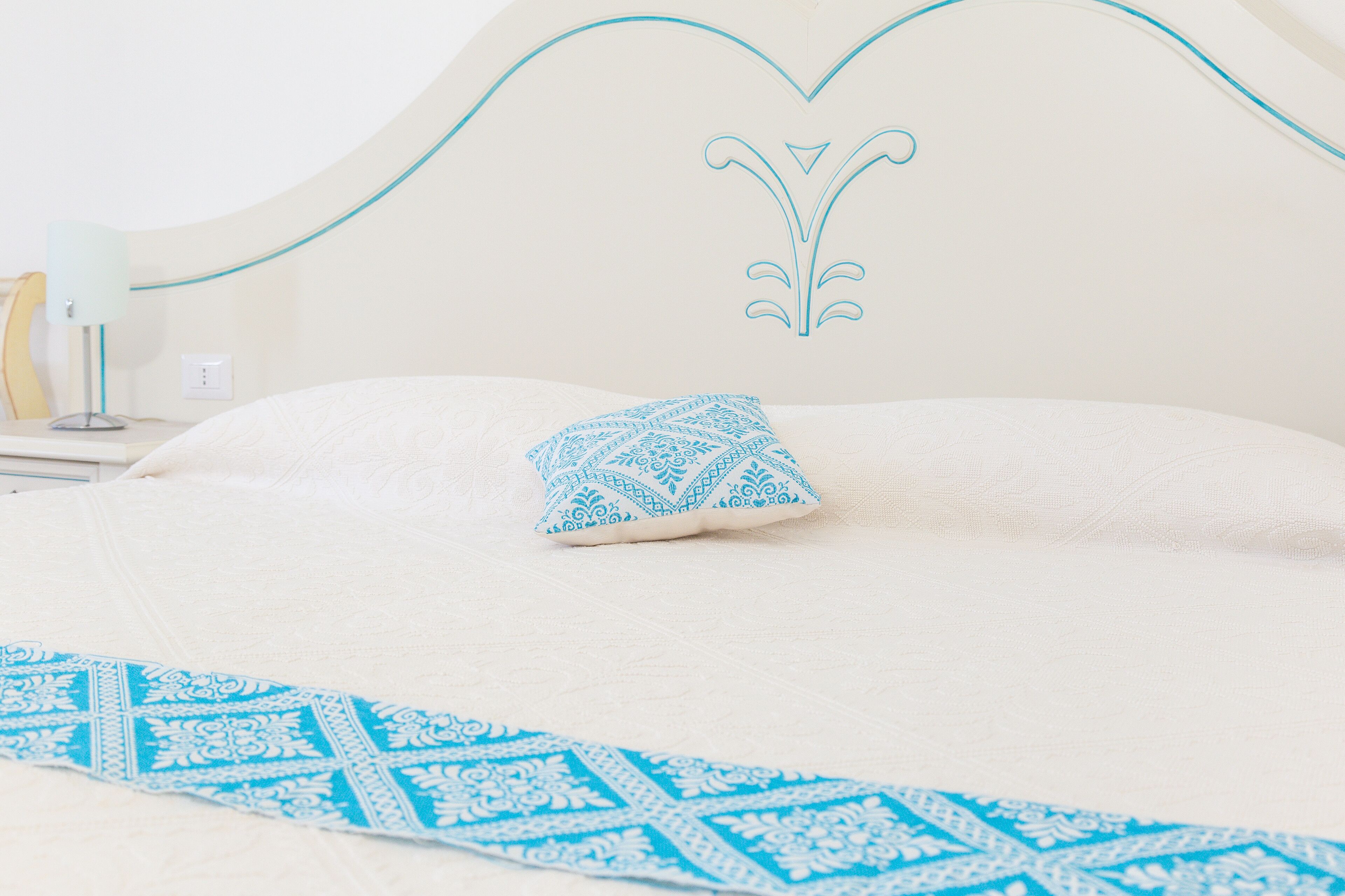 A neatly made bed with a patterned blue pillow and a matching blue runner.