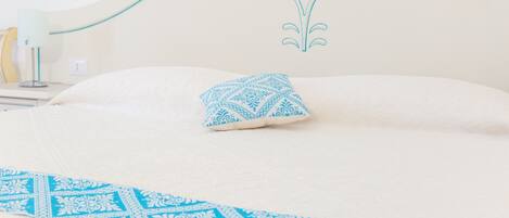 A neatly made bed with a patterned blue pillow and a matching blue runner.