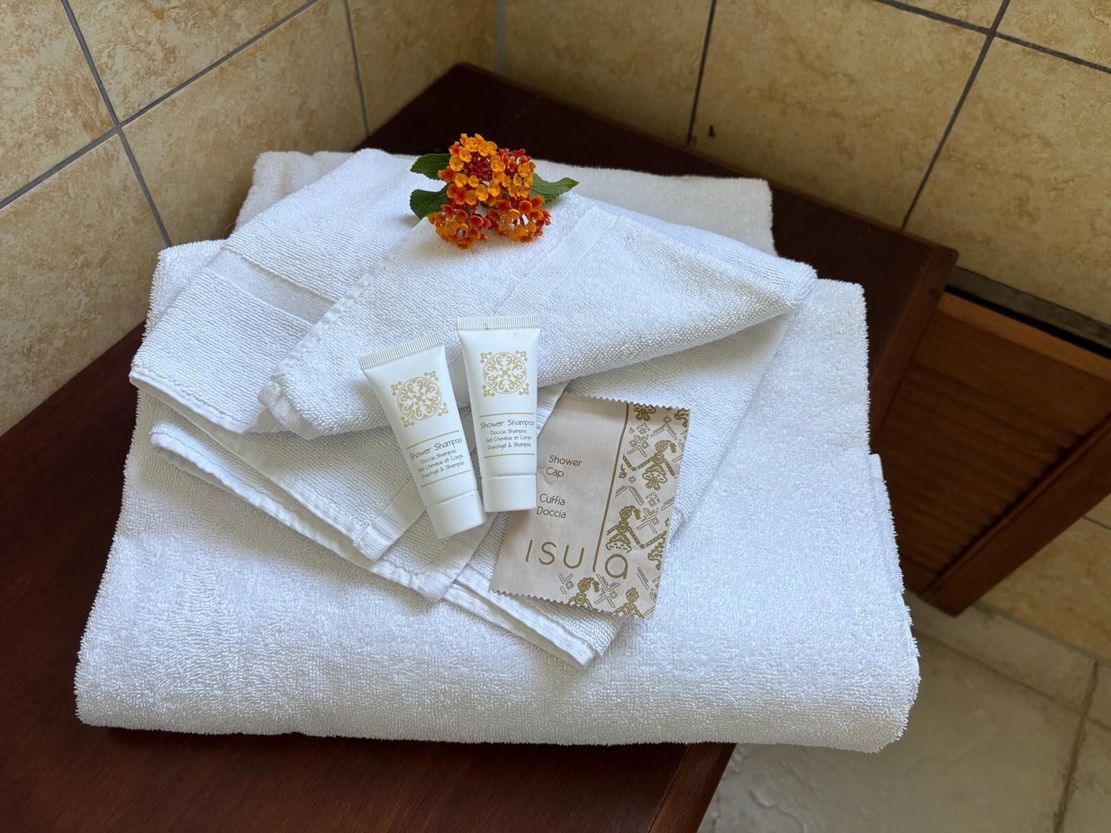 Un bagno con un asciugamano bianco, un piccolo fiore e due flaconi di articoli da toilette su un piano in legno.