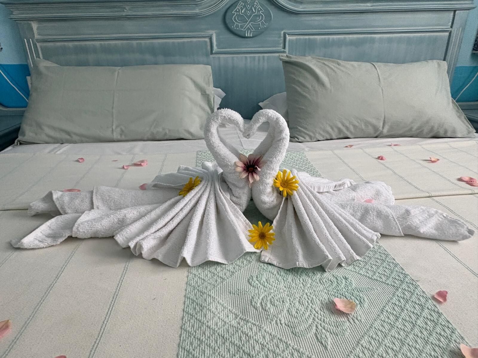 Una cama con una decoración de toallas en forma de cisnes, un tapete texturizado verde y un cabecero con un emblema circular.