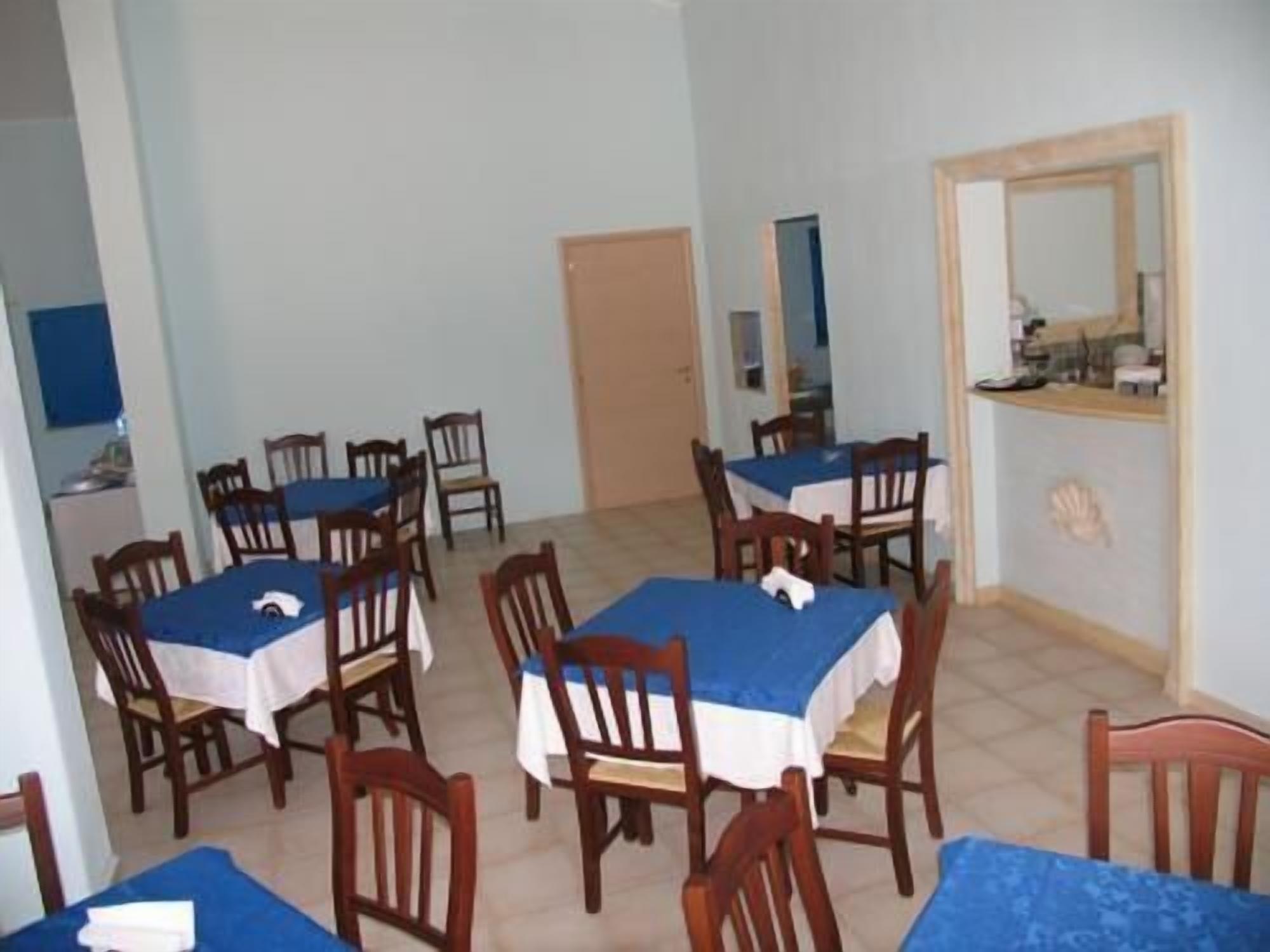 Un comedor con varias mesas y sillas, una zona de cocina con mostrador y una puerta que da a otra habitación.