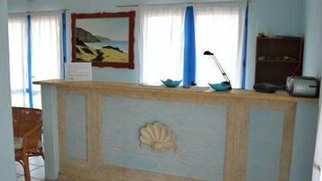 Un espace d’accueil avec un comptoir en bois, un tableau représentant un paysage et une lampe de bureau.