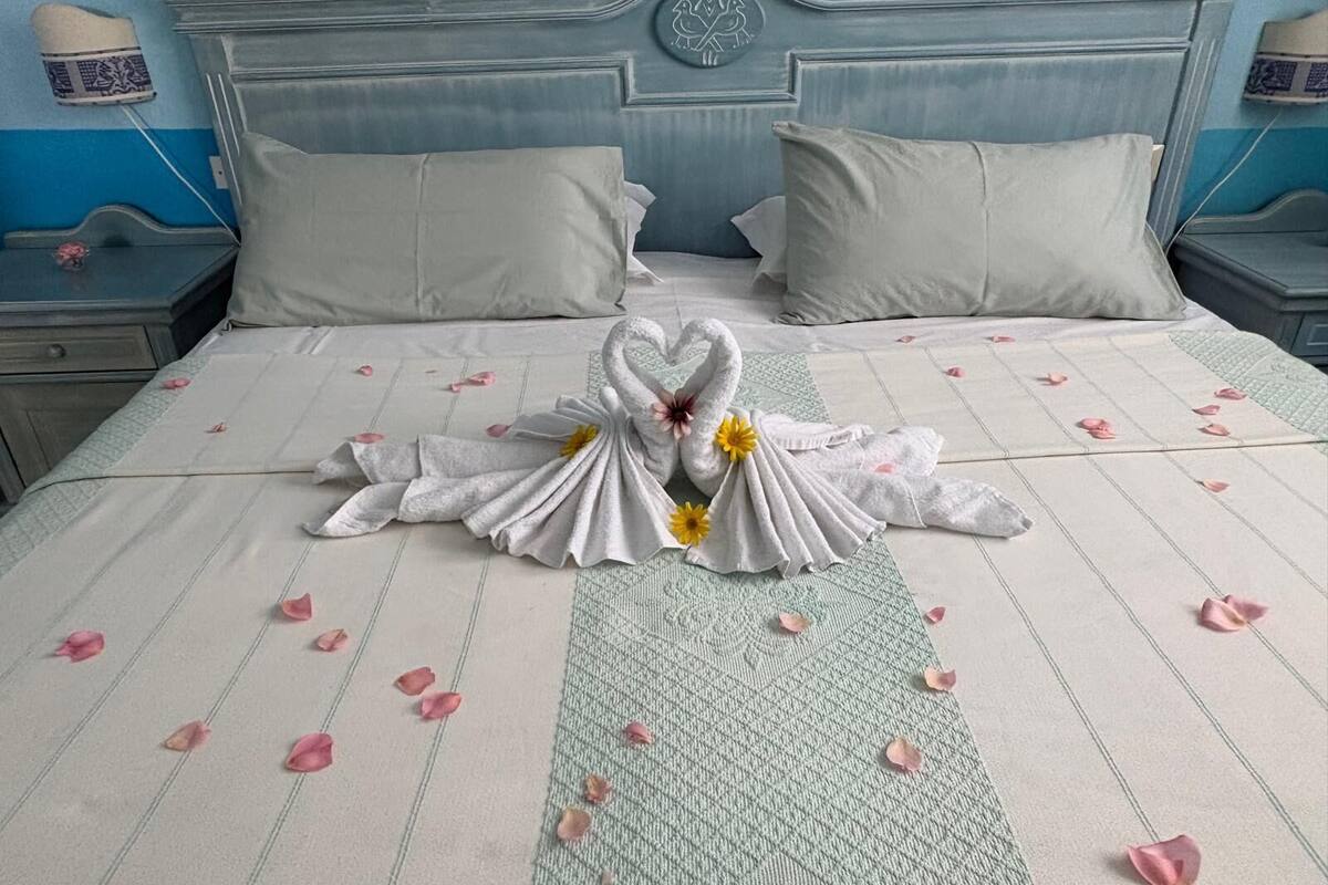 A neatly made bed with a swan towel design, pillows, and scattered rose petals.