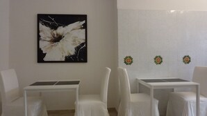 Una habitación con paredes blancas, un cuadro abstracto grande y tres mesas pequeñas con sillas blancas.