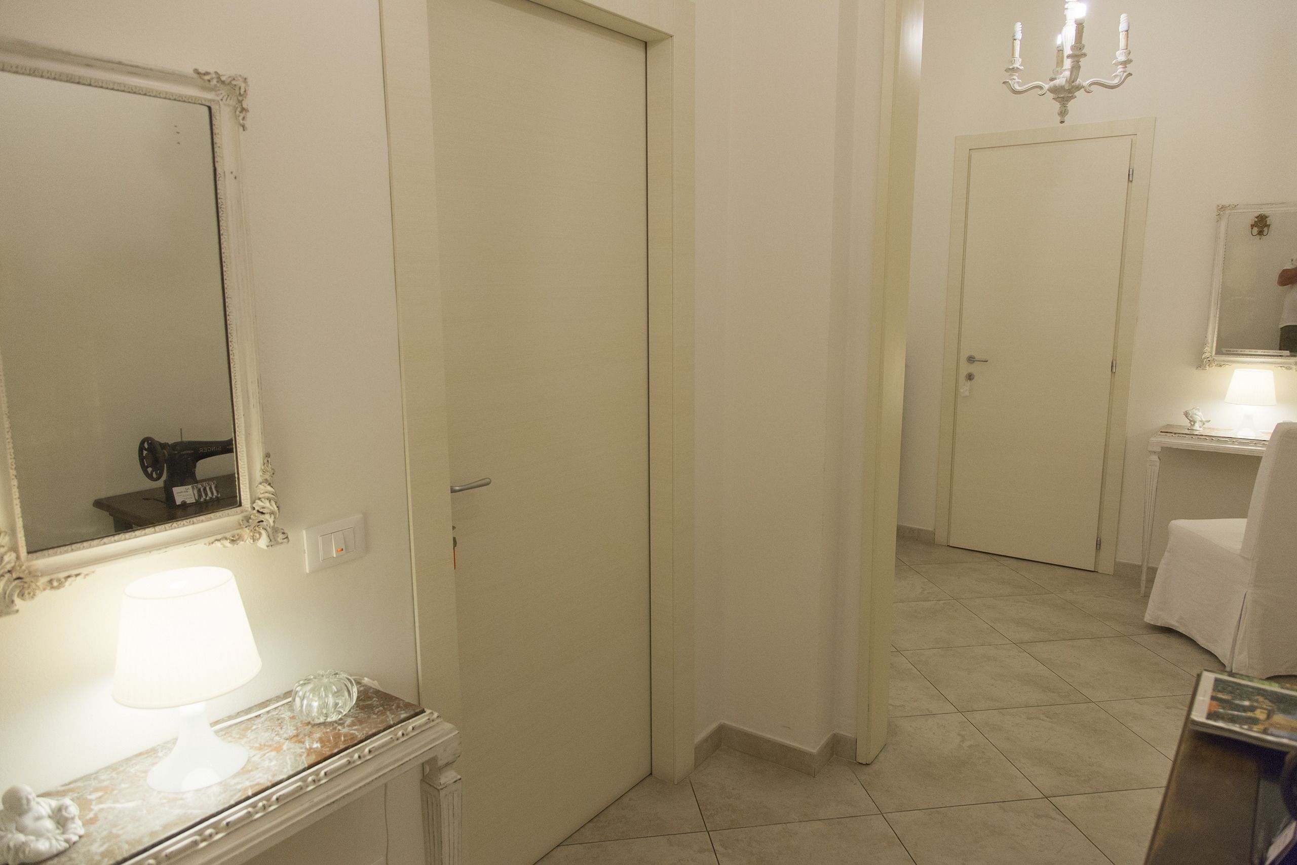 Un pasillo con un espejo, una lámpara y una puerta que da a otra habitación.