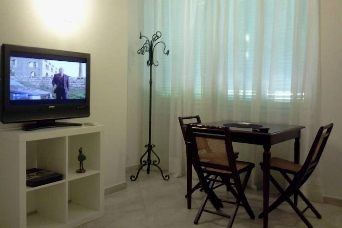 A living room with a television on a stand, a dining table with chairs, and a decorative iron stand.