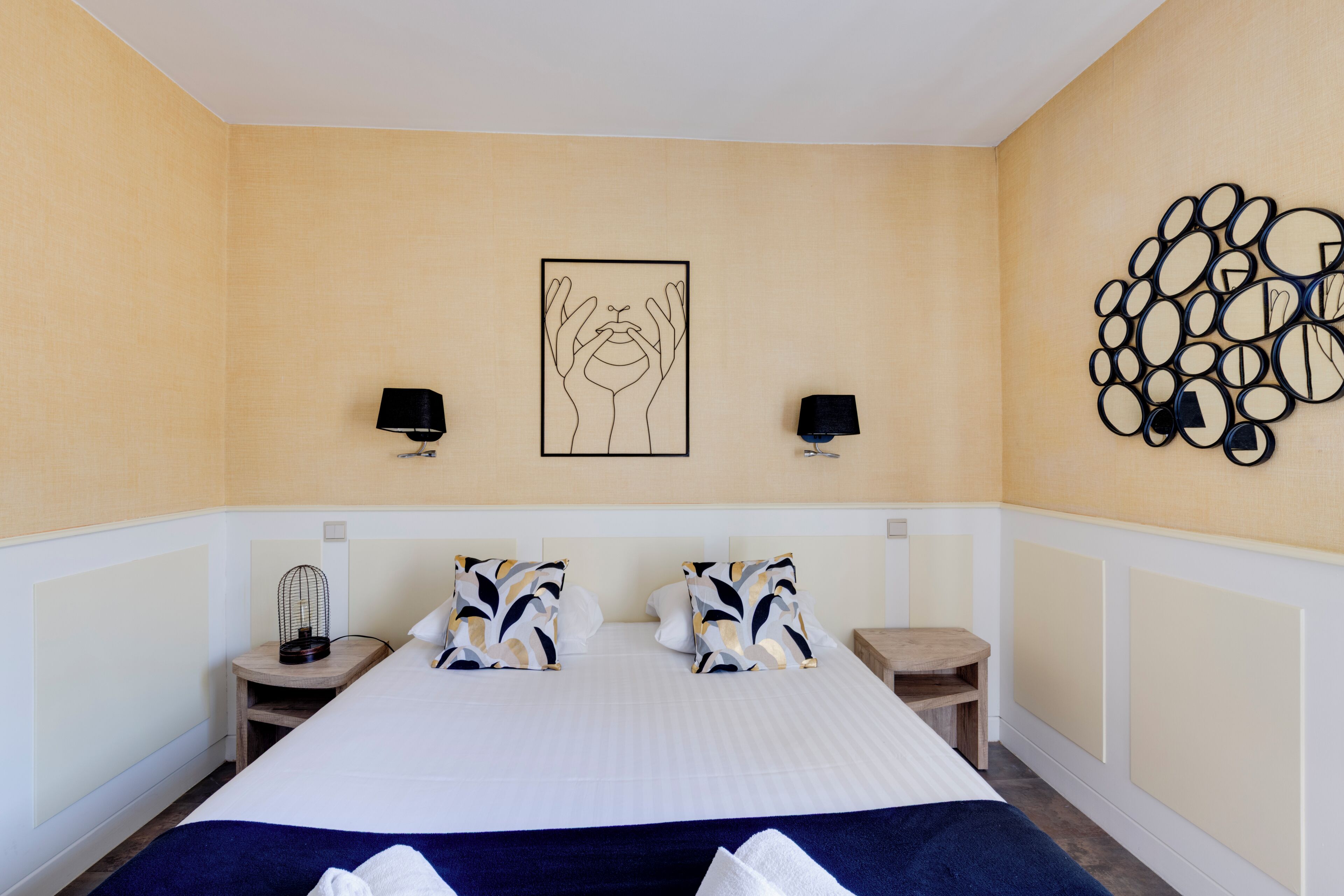 A hotel room with a large bed, two bedside tables, a wall art piece, and a decorative wall panel.