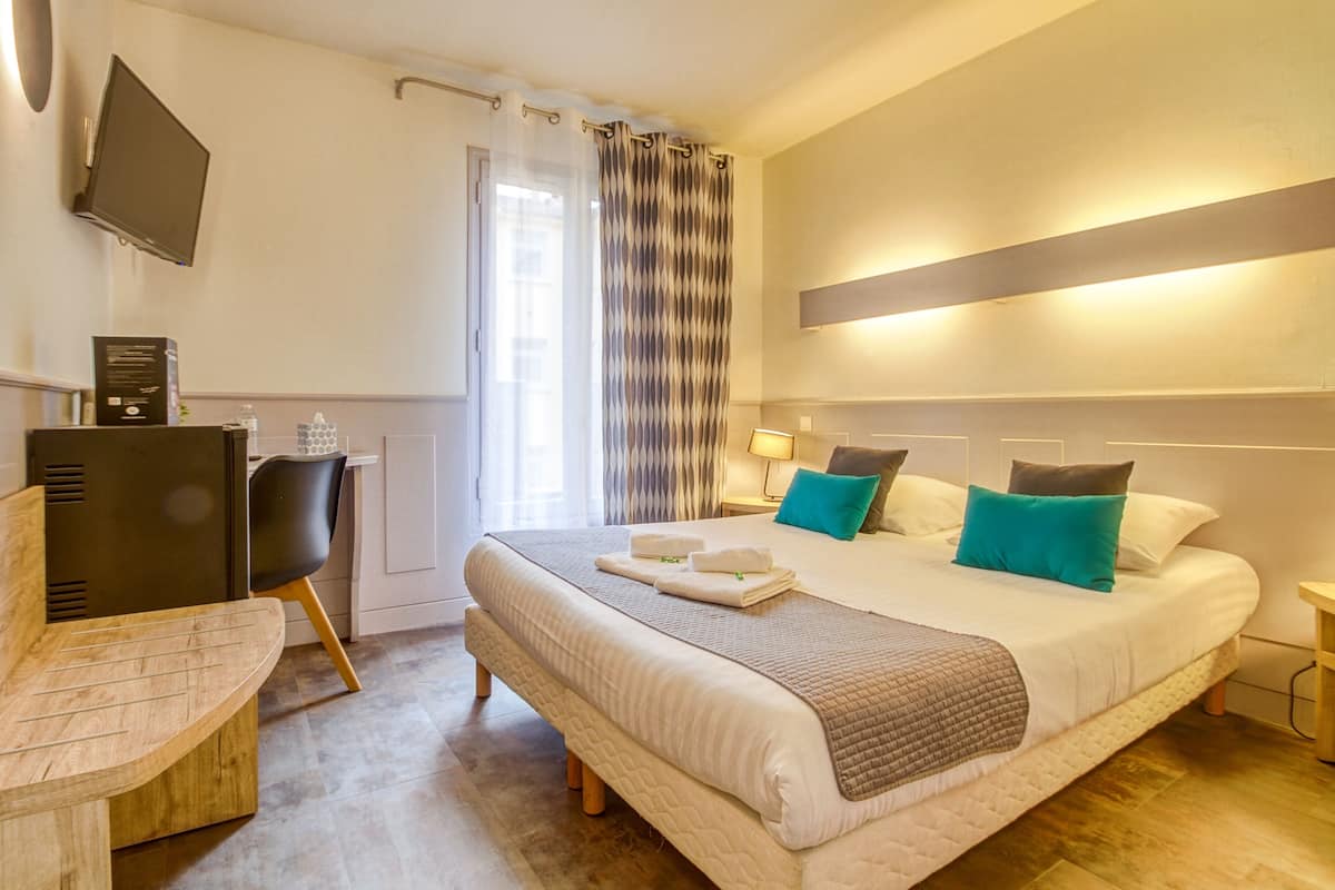 A hotel room with a bed, a desk, a chair, a TV, and a window with curtains.