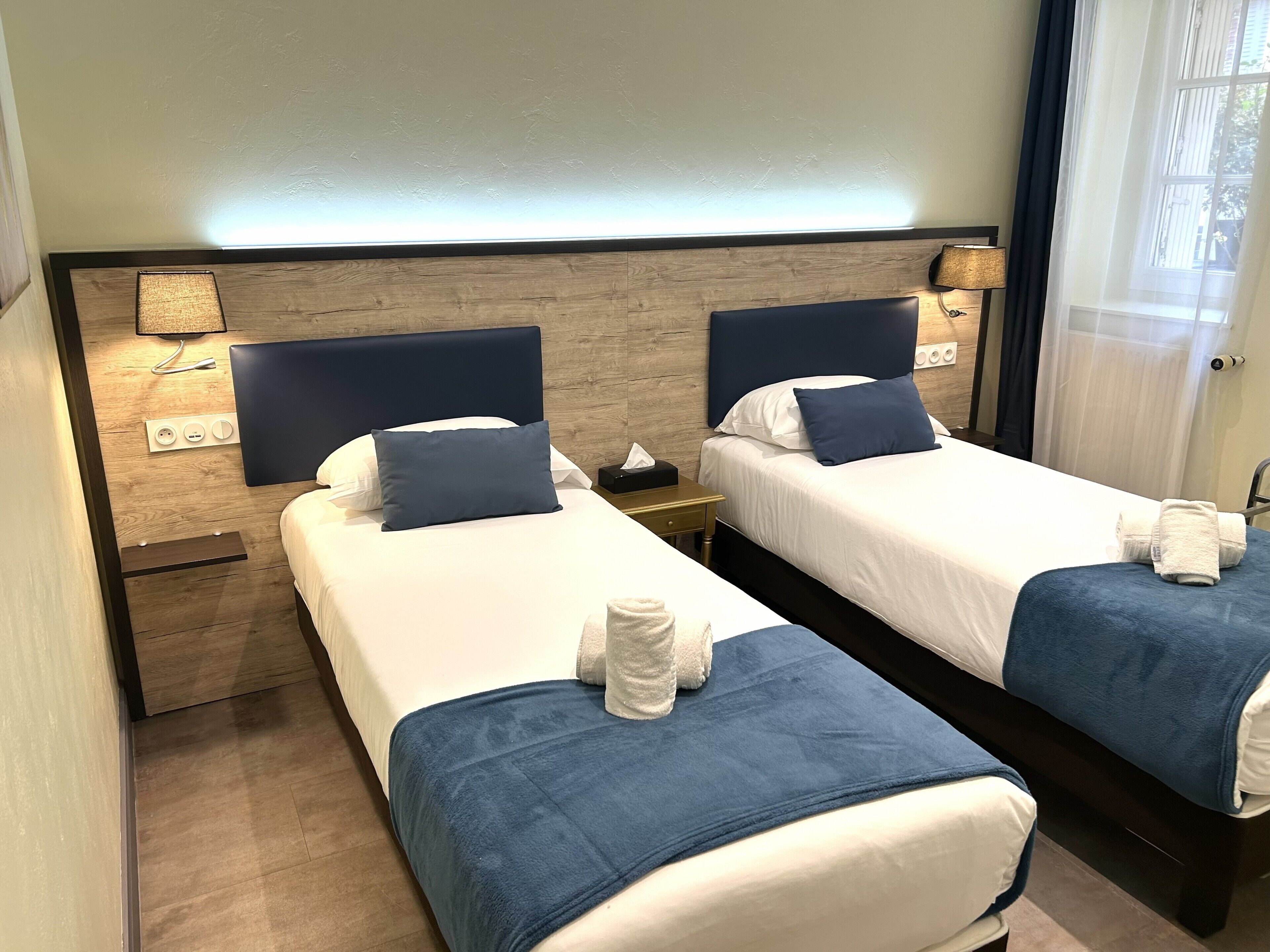 Habitación de hotel con dos camas, cada una con cabecera, mesitas de noche, lámparas y toallas.