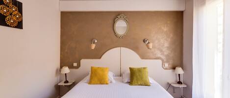 Habitación de hotel con una cama grande, dos lámparas de noche, un espejo y una lámpara de pared.
