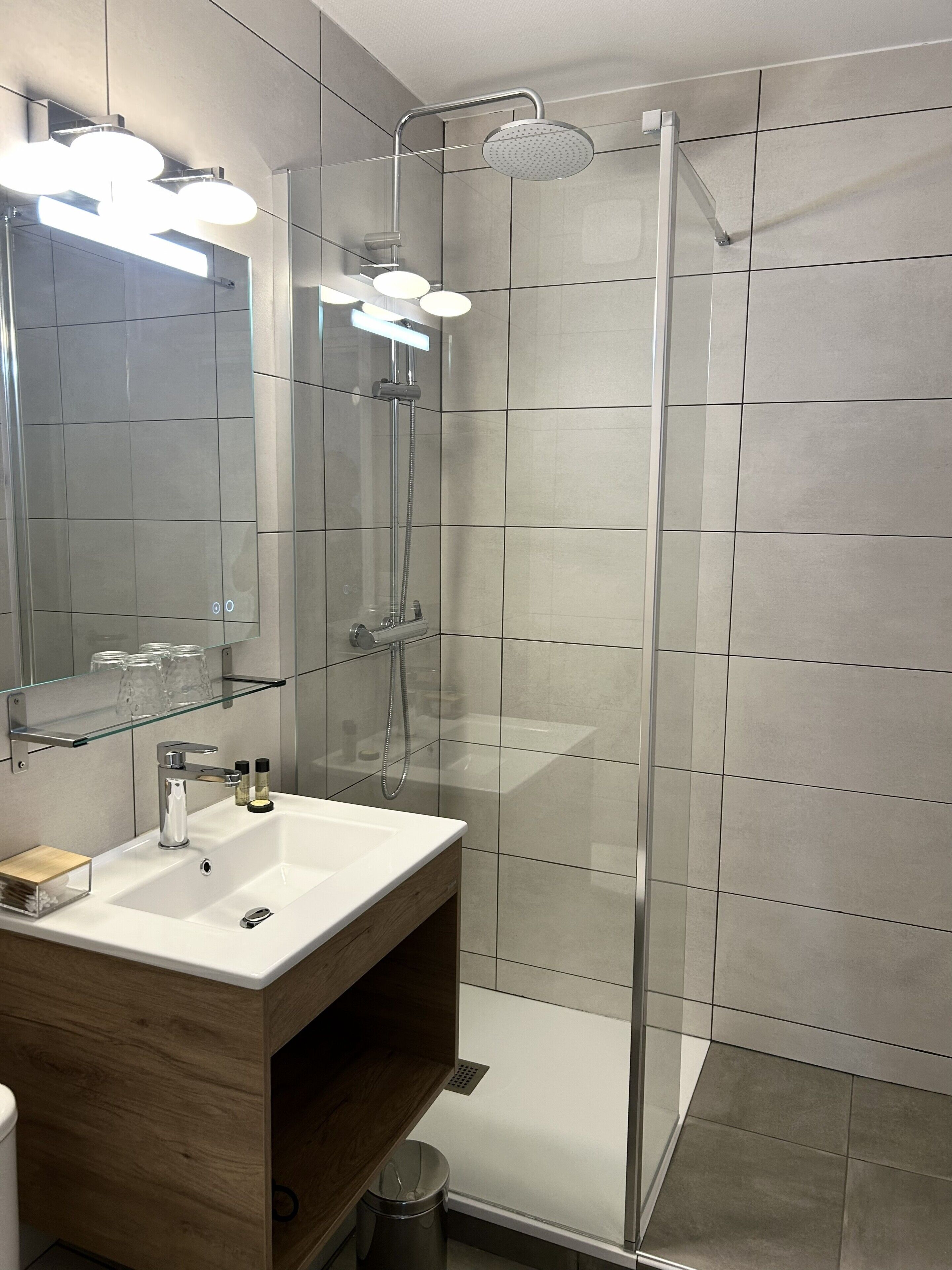 Een moderne badkamer met een douchecabine van glas, een houten wastafelmeubel met een wastafel en een spiegel erboven.