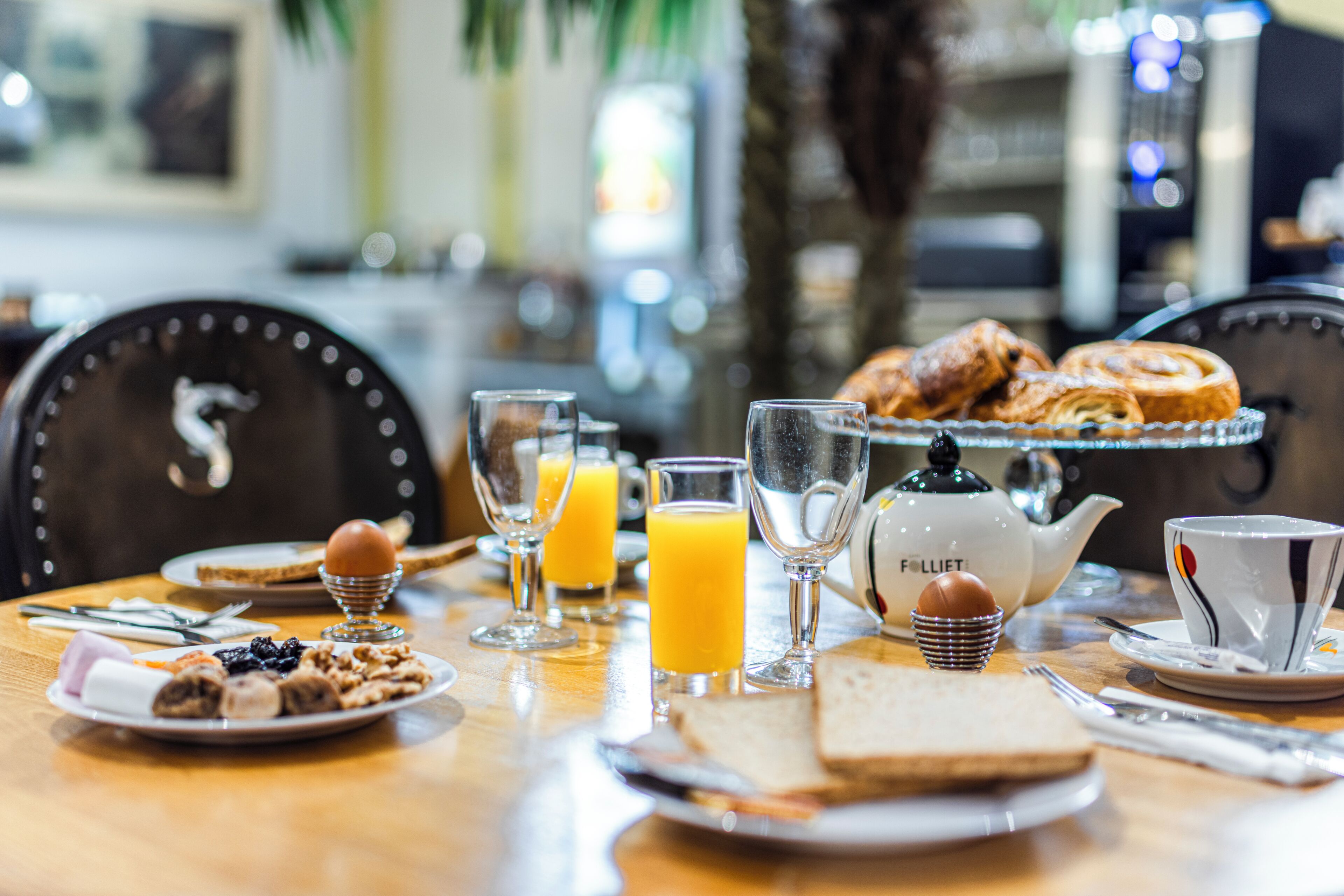 Una mesa de desayuno con platos de comida, vasos de jugo de naranja, un calentador de agua y una taza.
