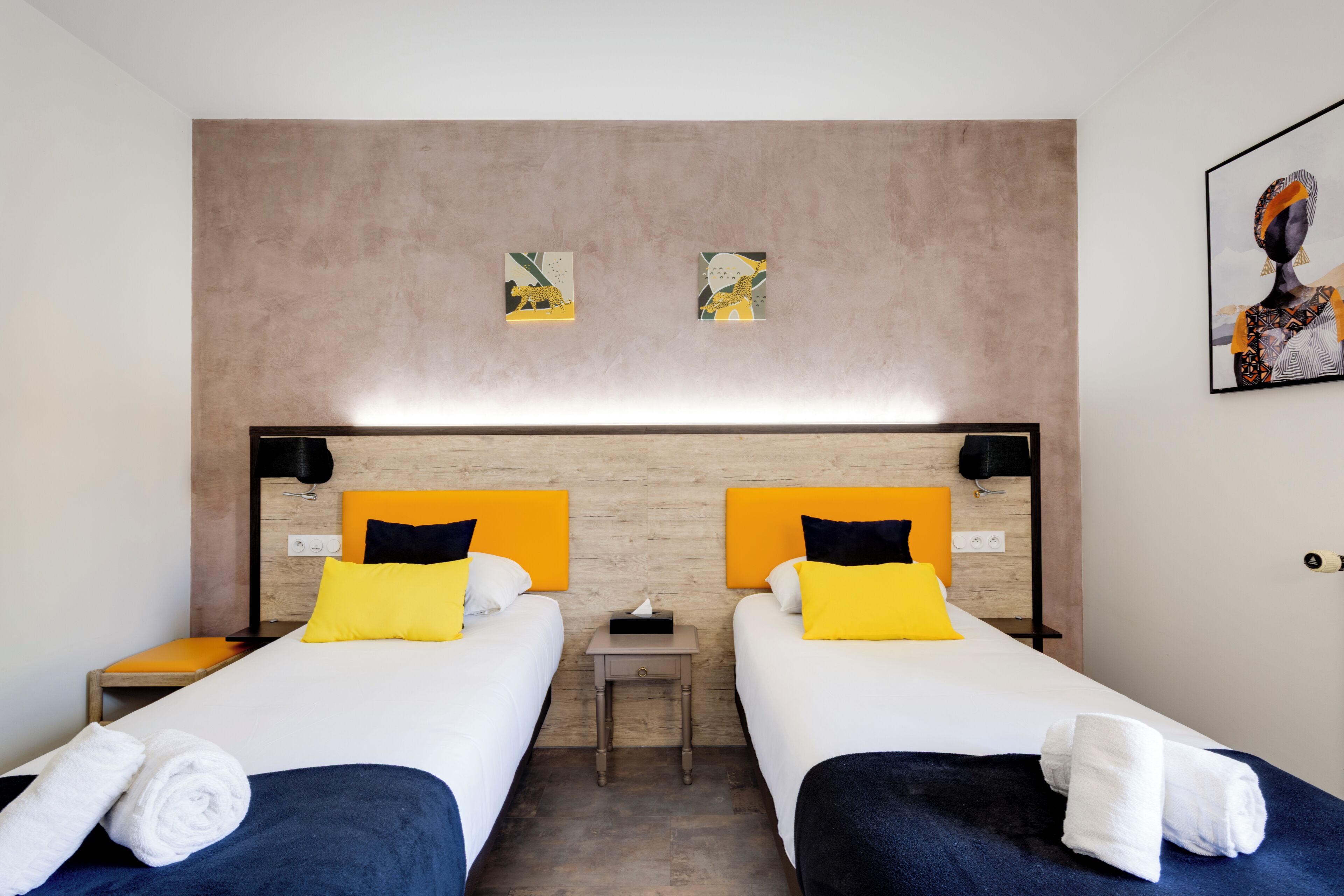 Habitación de hotel con dos camas, cada una con cabecera, mesita de noche y lámpara de pared.