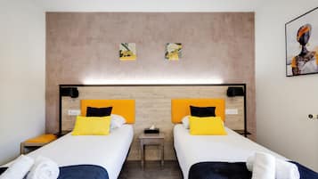 Habitación de hotel con dos camas, cada una con cabecera, mesita de noche y lámpara de pared.